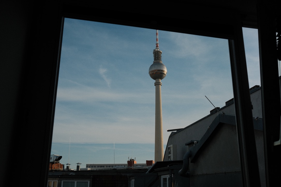 Berlin TV Tower framed through a window, rooftops below a clear sky
